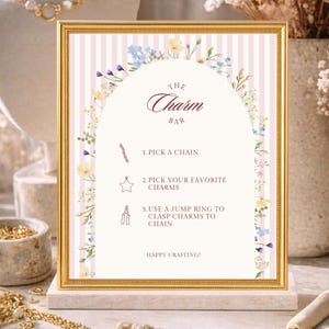 May include: A framed sign with gold trim and a pink and white striped background. The sign reads "The Charm Bar" and provides instructions for creating jewelry. Floral accents and the words "Happy Crafting!" complete the design.