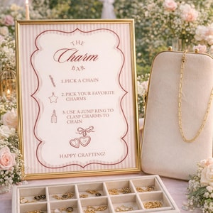 Könnte beinhalten: Ein goldgerahmtes Schild mit dem Text "The Charm Bar" und Anweisungen zur Herstellung von individuellem Schmuck. Eine Vitrine enthält verschiedene Charms, und eine goldene Kette hängt an einem cremefarbenen Ständer. Das Schild hat einen rosa-weiß gestreiften Hintergrund.
