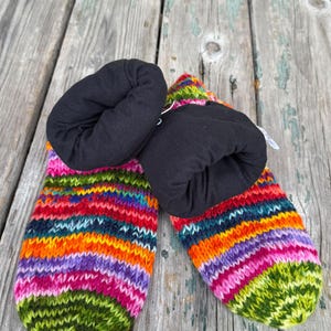 May include: A pair of knit slippers featuring a vibrant, multi-colored horizontal striped pattern in shades of green, pink, purple, orange, and blue. The slippers have a solid black fabric lining that extends to form a soft, folded cuff.