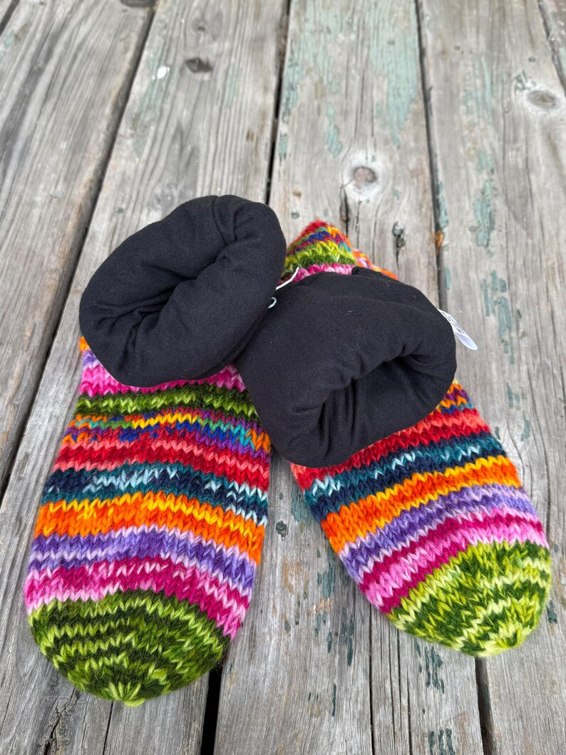 May include: A pair of knit slippers featuring a vibrant, multi-colored horizontal striped pattern in shades of green, pink, purple, orange, and blue. The slippers have a solid black fabric lining that extends to form a soft, folded cuff.