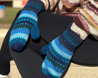 May include: Knitted mittens in various shades of blue, teal, and navy. The mittens have a striped pattern with a ribbed cuff and a thumb. These mittens are designed for warmth and comfort, perfect for cold weather.