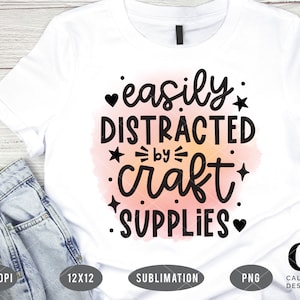 Puede incluir: Camiseta blanca con un fondo de acuarela rosa y texto negro que dice "f&aacute;cilmente distra&iacute;do por los suministros de manualidades".