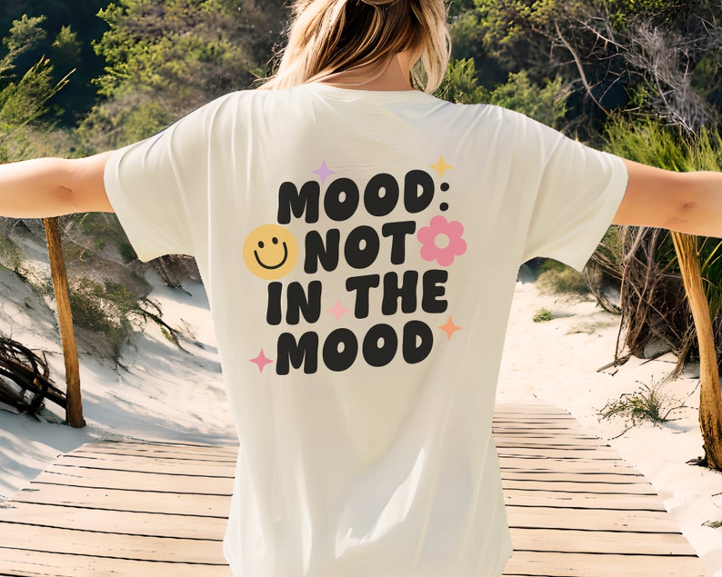 Pode incluir: Camiseta branca com um gr&aacute;fico preto que diz "Mood: Not in the Mood" com um rosto sorridente e uma flor rosa.