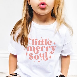 May include: White t-shirt with a pink graphic that says "little merry soul" with stars around the text.