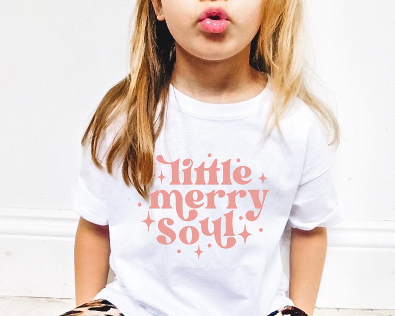 May include: White t-shirt with a pink graphic that says "little merry soul" with stars around the text.