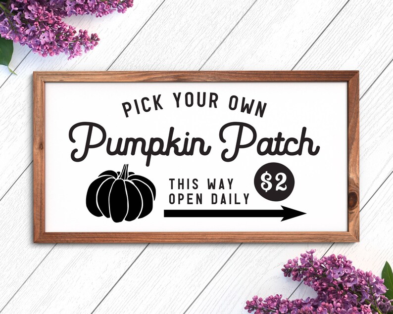 K&ouml;nnte beinhalten: Ein wei&szlig;es Schild mit einem braunen Holzrahmen, das einen K&uuml;rbis-Patch bewirbt. Das Schild lautet "Pick Your Own Pumpkin Patch" mit einer schwarzen Silhouette eines K&uuml;rbisses und einem Pfeil, der nach rechts zeigt. Der Text "This Way Open Daily" und "2&euro;" steht ebenfalls auf dem Schild.