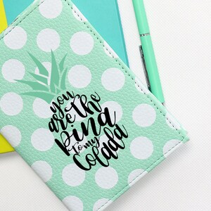 May include: A mint green passport holder with white polka dots and a pineapple graphic. The text "You are the pina to my colada" is printed on the holder.