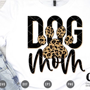 May include: A white t-shirt with black text that says "Dog Mom" with a leopard print paw print in the middle of the text.