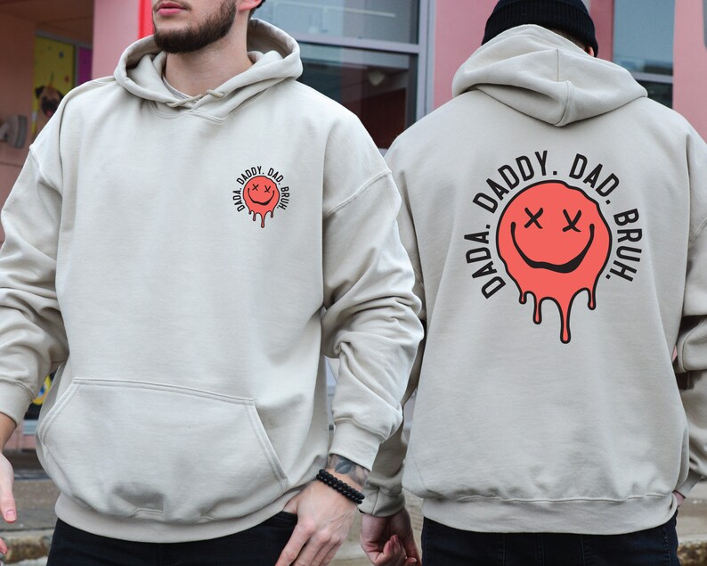 May include: A light beige hoodie with a black and red graphic on the front and back. The graphic is a dripping smiley face with the text "DADA. DADDY. DAD. BRUH." around it.