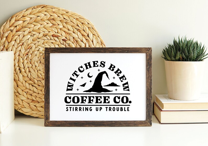 May include: A framed print with a black and white design of a witch's hat, crescent moon, and stars. The text reads "Witches Brew Coffee Co. Stirring Up Trouble".