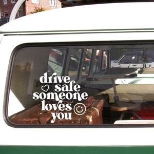 May include: White vinyl sticker with the text "drive safe someone loves you" with a heart and smiley face. The sticker is on the back window of a green van.