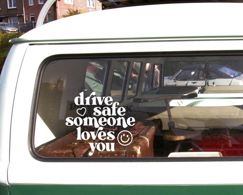 May include: White vinyl sticker with the text "drive safe someone loves you" with a heart and smiley face. The sticker is on the back window of a green van.