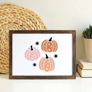 May include: A framed print with three stylized pumpkins with stars and moons. The pumpkins are in shades of orange and pink.