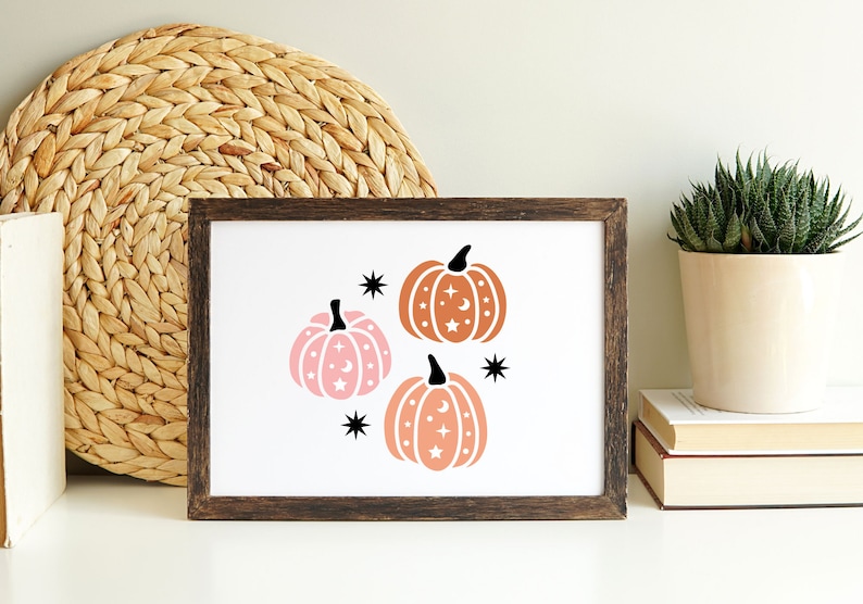 May include: A framed print with three stylized pumpkins with stars and moons. The pumpkins are in shades of orange and pink.