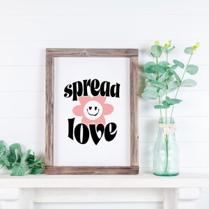 May include: A framed print with a pink flower with a smiley face and the text "spread love" in black letters.