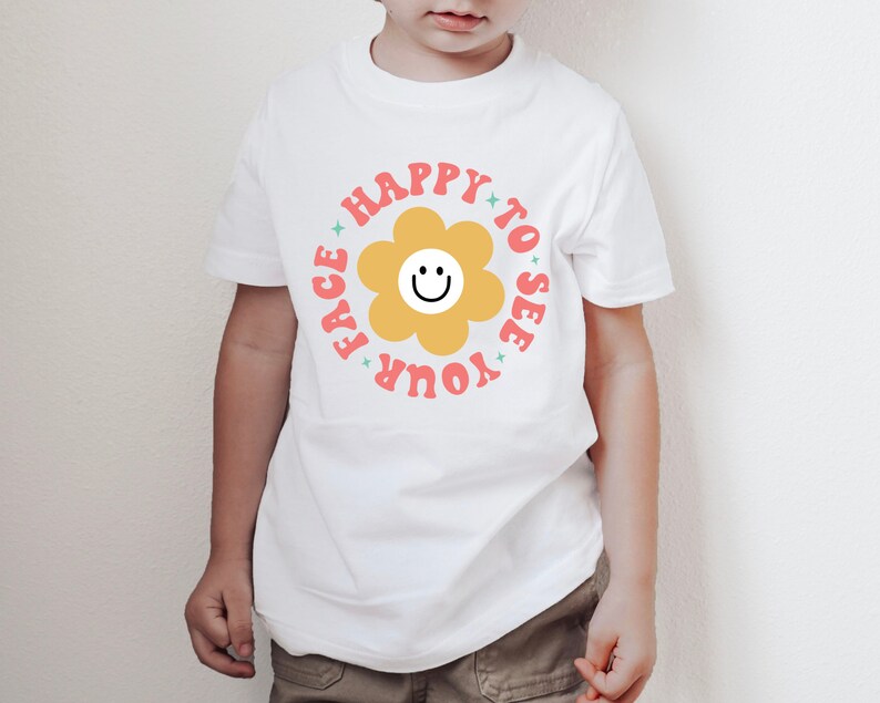 May include: White t-shirt with a pink and yellow flower graphic and the text "Happy to see your face".