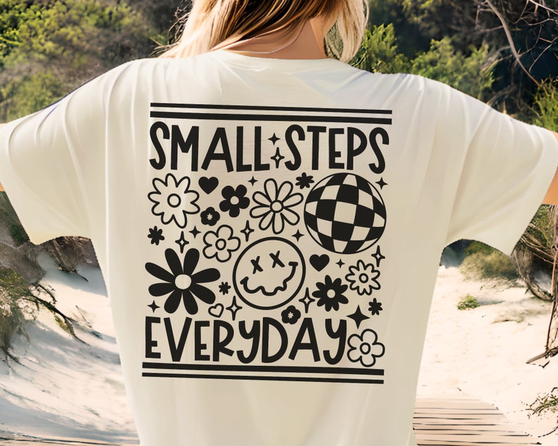 K&ouml;nnte beinhalten: Ein wei&szlig;es T-Shirt mit einem schwarzen Grafikdesign, auf dem "SMALL STEPS EVERYDAY" steht, umgeben von Blumen, einem Smiley und einer Discokugel.