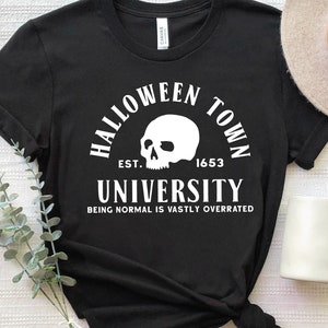 May include: Black t-shirt with white text that reads "Halloween Town University Est. 1653 Being Normal Is Vastly Overrated". A skull graphic is above the text.