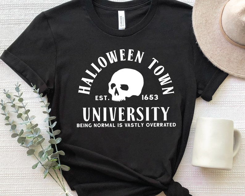 May include: Black t-shirt with white text that reads "Halloween Town University Est. 1653 Being Normal Is Vastly Overrated". A skull graphic is above the text.