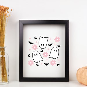 May include: A framed print with a white background and a repeating pattern of pink flowers, black bats, white ghosts, and crescent moons.