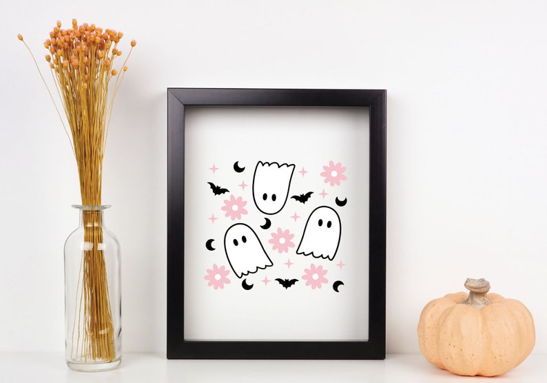 May include: A framed print with a white background and a repeating pattern of pink flowers, black bats, white ghosts, and crescent moons.
