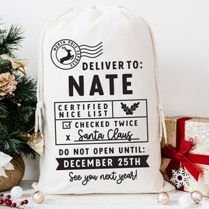May include: A white canvas Santa sack with black text that reads "Deliver to: NATE Certified Nice List ☑ Checked Twice x Santa Claus Do Not Open Until: December 25th See you next year!"