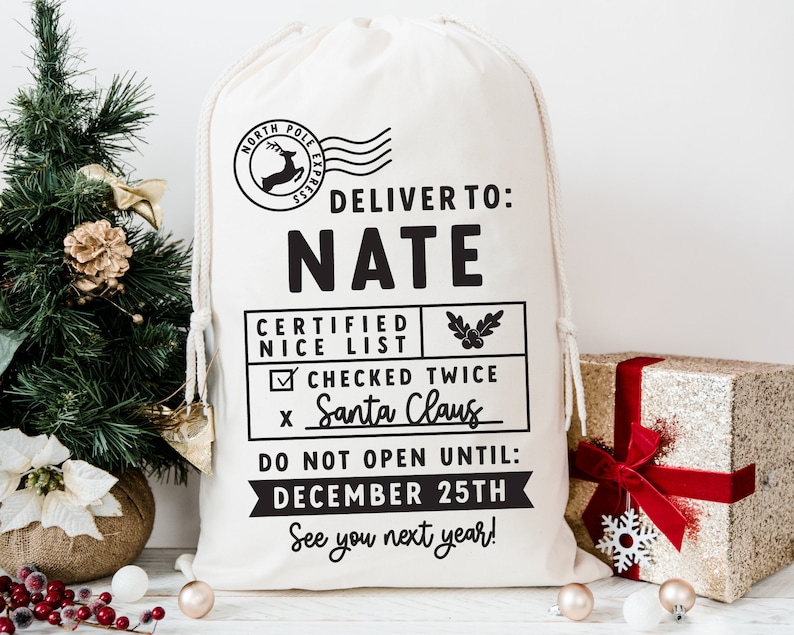May include: A white canvas Santa sack with black text that reads "Deliver to: NATE Certified Nice List ☑ Checked Twice x Santa Claus Do Not Open Until: December 25th See you next year!"