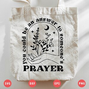 K&ouml;nnte beinhalten: Eine wei&szlig;e Einkaufstasche mit schwarzem Text, der "You could be an answer to someone's prayer." lautet. Der Text ist in einer stilisierten Schriftart gehalten und von einem schwarzen Halbmond und einem floralen Design umgeben.