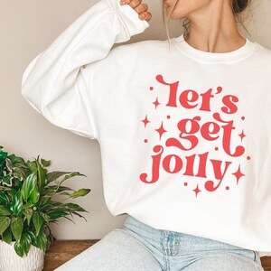May include: White sweatshirt with a red graphic that says "Let's get jolly" with stars around the text.