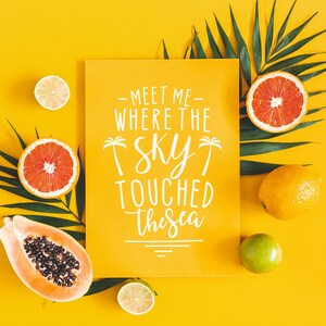 K&ouml;nnte beinhalten: Ein gelber Hintergrund mit einer wei&szlig;en Karte, auf der "Meet me where the sky touched the sea" steht. Die Karte ist von Palmbl&auml;ttern, Zitronen, Limetten und Grapefruits umgeben.