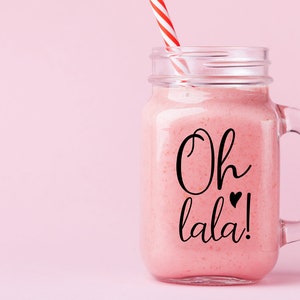 K&ouml;nnte beinhalten: Ein rosa Smoothie in einem durchsichtigen Glas-Mason-Glas mit einem rot-wei&szlig; gestreiften Strohhalm. Das Glas hat einen schwarzen Griff und den Text "Oh lala!" mit zwei kleinen Herzen.