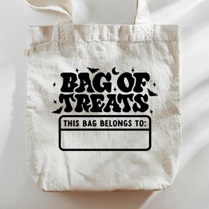 K&ouml;nnte beinhalten: Eine wei&szlig;e Stofftasche mit schwarzem Text, der in einer Retro-Schriftart "Bag of Treats" lautet. Die Tasche hat auch ein schwarzes Rechteck mit dem Text "This bag belongs to:" und einen leeren Platz zum Schreiben eines Namens.