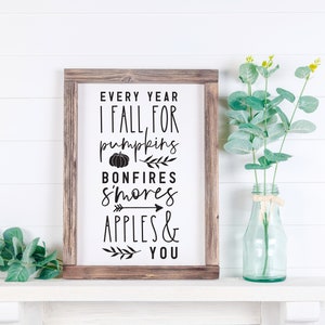 K&ouml;nnte beinhalten: Ein rustikales Holzschild mit dem Text "Every year I fall for pumpkins, bonfires, s'mores, apples & you" in schwarzer Schrift. Das Schild ist mit einer kleinen K&uuml;rbisgrafik, einem kleinen Pfeil und einem kleinen Zweig mit Bl&auml;ttern verziert.