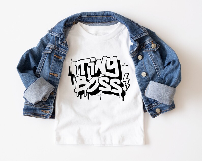 May include: White t-shirt with a black graphic that says "TINY BOSS" in a graffiti style with drips and lightning bolts.