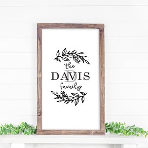 May include: A framed sign with a black and white floral wreath design. The sign reads "The Davis Family" with a stylized letter "D" in the center.