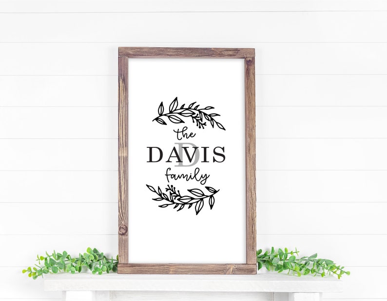 May include: A framed sign with a black and white floral wreath design. The sign reads "The Davis Family" with a stylized letter "D" in the center.
