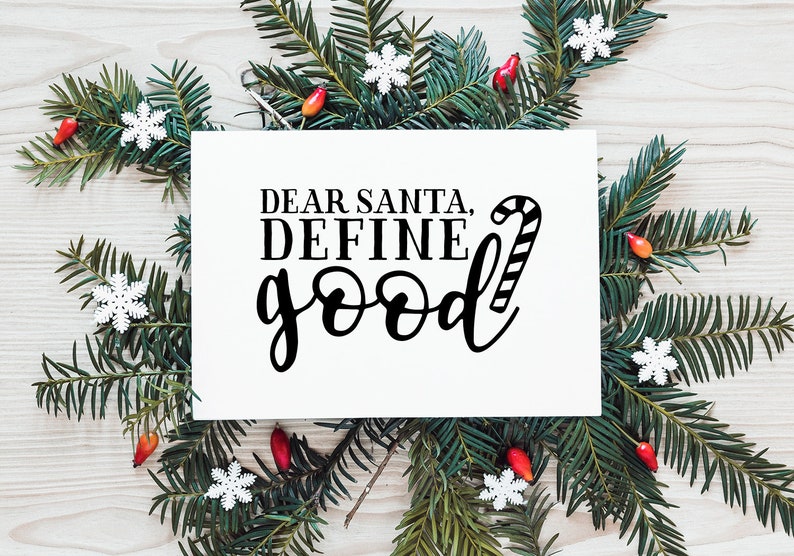 May include: A white card with black text that reads "Dear Santa, Define Good" with a candy cane graphic next to the text. The card is surrounded by green pine branches with red berries and white snowflakes.