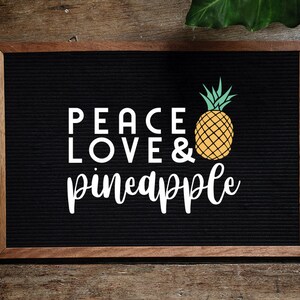 May include: A black letter board with a wooden frame, displaying the text "Peace Love & pineapple" in white letters. A yellow pineapple with green leaves is pictured next to the text.