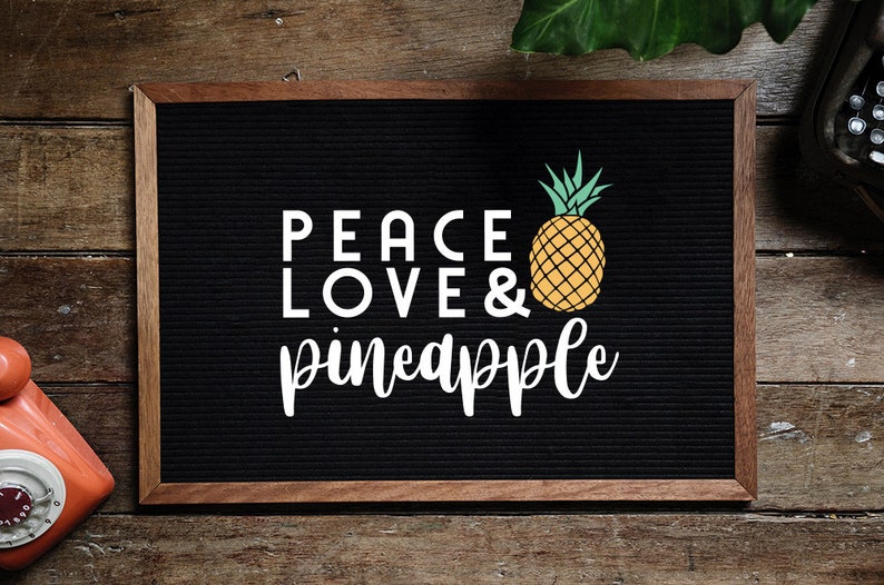 May include: A black letter board with a wooden frame, displaying the text "Peace Love & pineapple" in white letters. A yellow pineapple with green leaves is pictured next to the text.