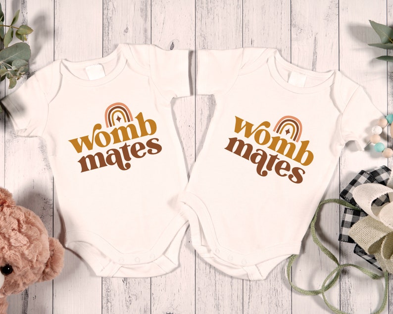 May include: Two white baby onesies with brown text that reads "womb mates" and a rainbow graphic.