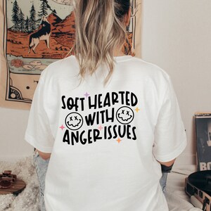 Pode incluir: Camiseta branca com um gr&aacute;fico preto que diz "Soft Hearted With Anger Issues" e dois rostos sorrindo com X para os olhos.