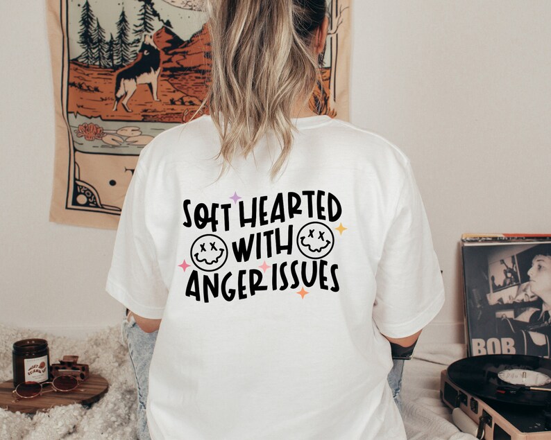 Pode incluir: Camiseta branca com um gr&aacute;fico preto que diz "Soft Hearted With Anger Issues" e dois rostos sorrindo com X para os olhos.