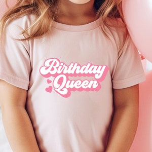 Op de afbeelding: Een roze T-shirt met de tekst "Birthday Queen" in roze en witte retro-lettertype.