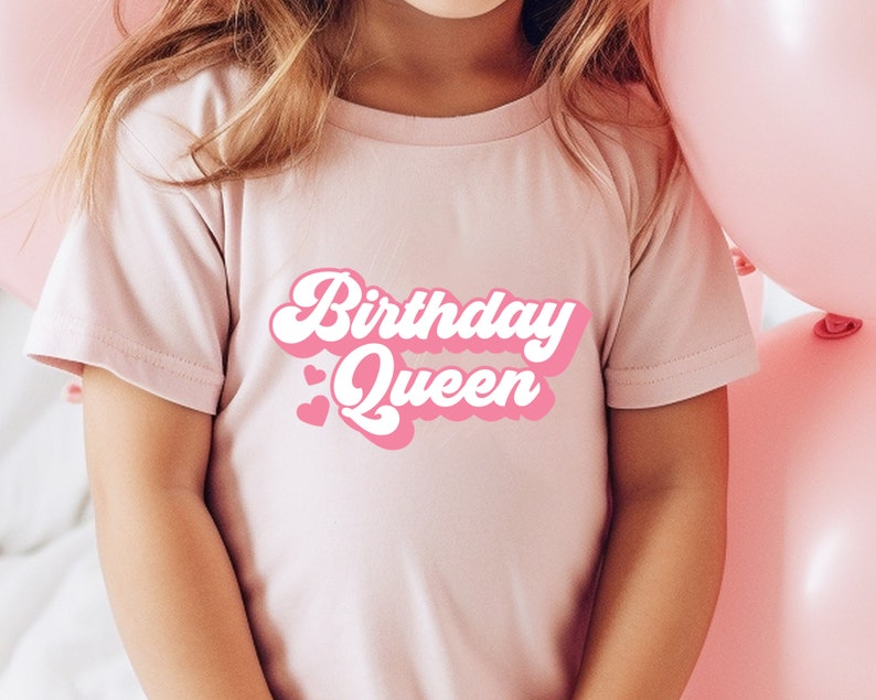 Op de afbeelding: Een roze T-shirt met de tekst "Birthday Queen" in roze en witte retro-lettertype.