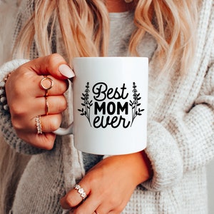 May include: White ceramic mug with black text that reads "Best Mom Ever" and a floral design.