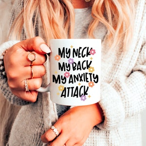Pode incluir: Caneca de cer&acirc;mica branca com texto preto que diz "My neck, my back, my anxiety attack" com pequenas ilustra&ccedil;&otilde;es de flores.