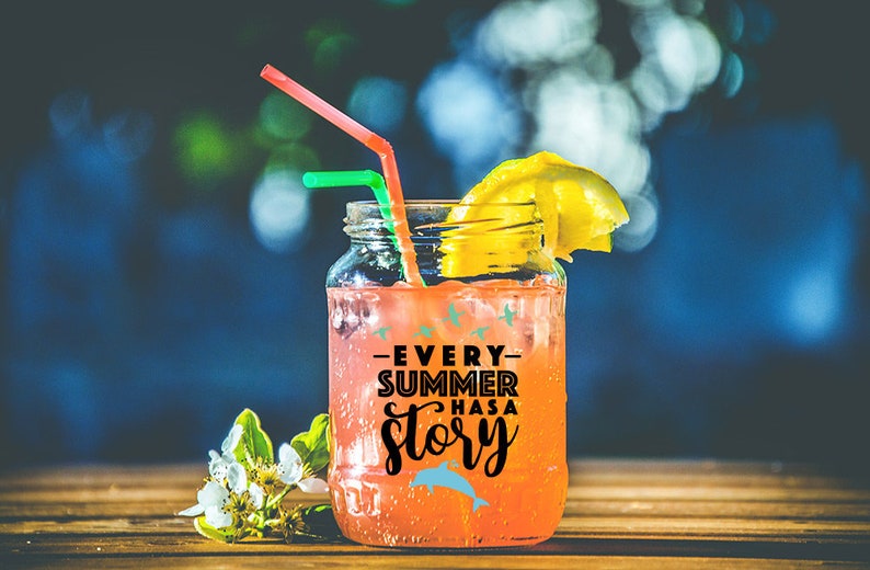 May include: A mason jar filled with a pink drink and a lemon wedge. The jar has a black and white sticker that says "Every Summer Has A Story" with a blue dolphin graphic.