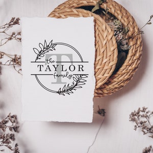 May include: A white card with a black and white logo design featuring a circle with a floral wreath and the text "the TAYLOR family" inside.