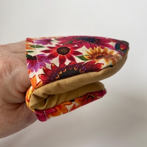 May include: A floral oven mitt with a tan interior and a vibrant pattern of red, pink, and yellow flowers on a cream background. The mitt is folded, showcasing the contrasting colours and textures.