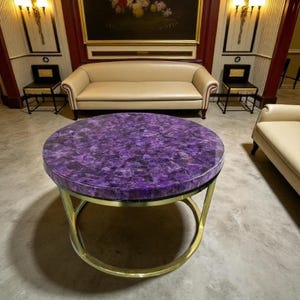 Könnte beinhalten: Runder Couchtisch mit einer leuchtend lila Amethyst-Oberfläche und einem goldfarbenen Metallgestell. Der Tisch hat eine polierte Oberfläche und ist ein Blickfang für jedes Wohnzimmer. Der Tisch hat einen Durchmesser von ca. 91 cm.